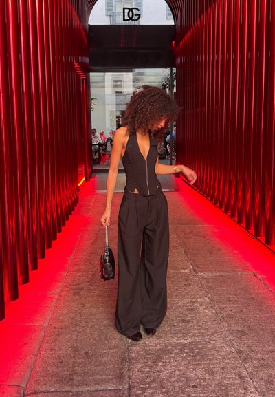 Mono negro con cremallera frontal, cuello alto y cortes laterales, combinado con pantalones negros de pierna ancha y un pequeño bolso negro.