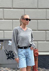 Sivkasta pletena majica z V-izrezom, svetlo modri jeans kratki hlače in črn pas. Dodatki vključujejo majhne obročaste uhane in črna sončna očala.