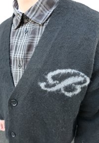 Cardigan noir en maille texturée, avec un logo brodé gris sur le côté gauche et une fermeture à boutons sur le devant.