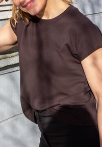 Hnedý krátky rukáv top z jemného, hladkého materiálu, s okrúhlym lemom a voľným strihom. Čierne nohavice s detailom zipsu v oblasti pásu.