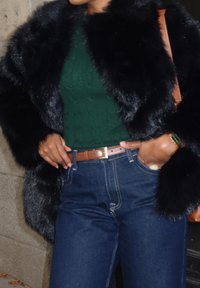 Mustaharha musta karvavilla takki, vihreä palmikkoneule, ruskea vyö kultaisilla yksityiskohdilla ja tummansiniset farkut esittelevät rentoa asua.