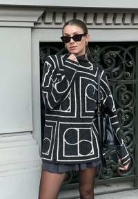 Maglione oversize in bianco e nero a fantasia con collo alto, maniche lunghe e finitura testurizzata. Abbinato a una borsa nera e una gonna grigia.