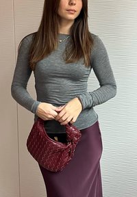 Bordeauxfarbene Gewebetasche mit einem geknoteten Griff. Langärmliges graues Oberteil und tief lila Rock. Glatte Textur und strukturiertes Design.