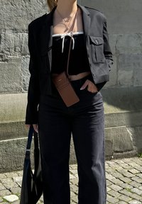 Musta bleiseri mustan lyhyen topin päällä, jossa on valkoinen naru, yhdistettynä korkeavyötäröisiin mustiin farkkuihin. Ruskea puhelinkotelo crossbody-muodossa. Musta laukku.
