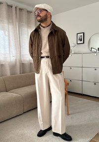 Chemise oversize marron, pull en tricot beige, pantalon large crème, chaussures noires et casquette blanche. La pièce présente des textures douces et des couleurs neutres.