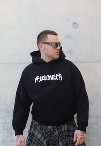 Svart hettegenser med hvitt logotrykk, med frontlomme og rutete detaljer under. Grå bakgrunn med glatt tekstur.