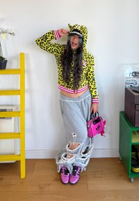 Dzeltenas leoparda raksta cropped kapuce ar rozā akcentiem, pelēkas nolietotas sporta bikses, rozā roku soma un spīdīgas rozā kurpes.