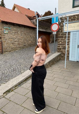 Top sin mangas con un diseño transparente y patrones abstractos, combinado con pantalones de pierna ancha negros de talle alto y zapatillas.