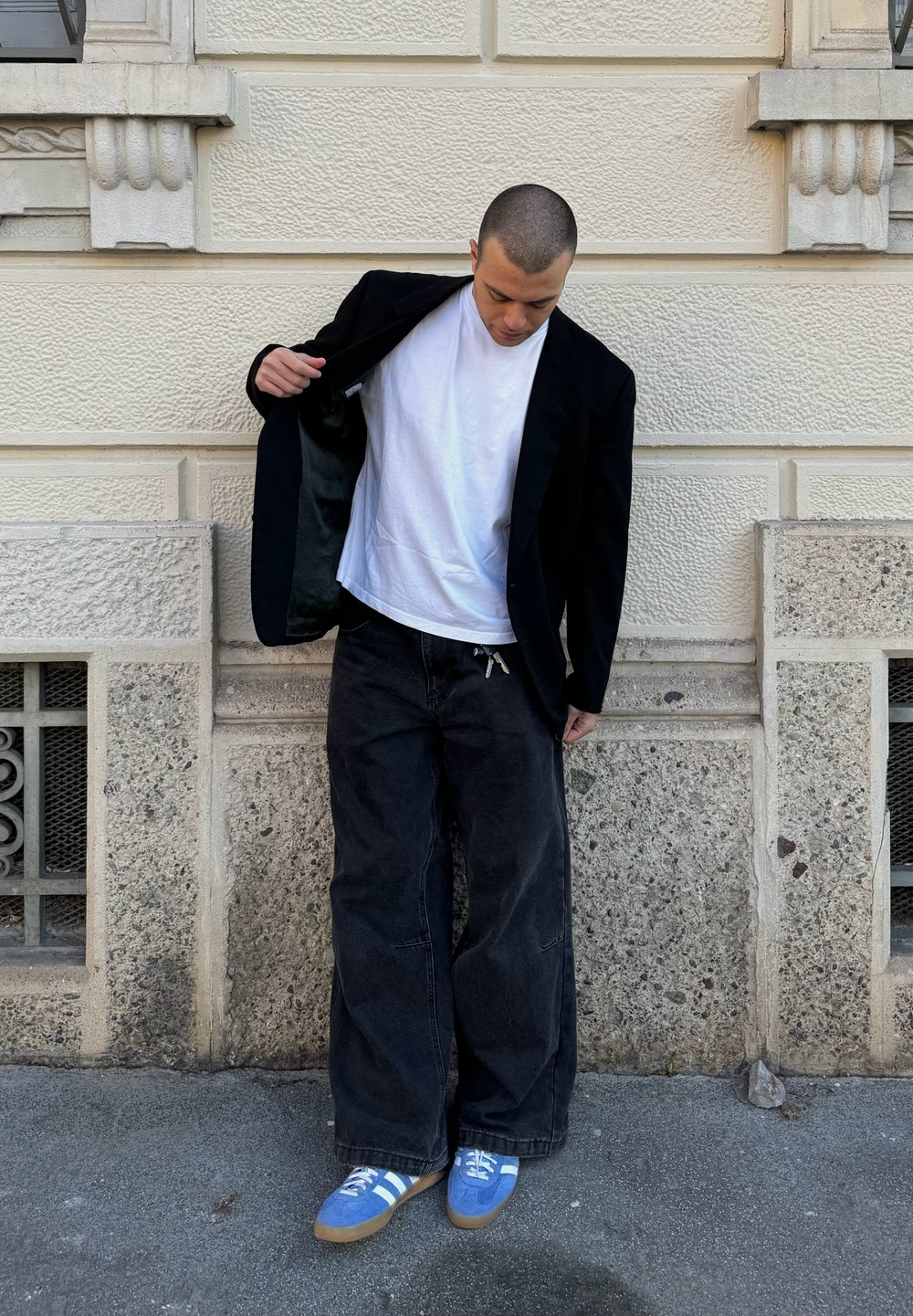 Blazer preto sobre uma t-shirt branca, combinado com jeans pretos largos e ténis azuis com riscas brancas. Texturas suaves e cores contrastantes.