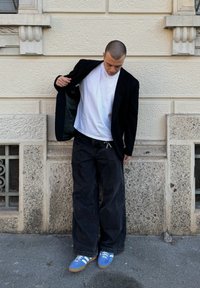 Blazer preto sobre uma t-shirt branca, combinado com jeans pretos largos e ténis azuis com riscas brancas. Texturas suaves e cores contrastantes.