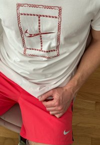 T-shirt branca com um padrão de corrente vermelha e o logo da Nike na frente, combinada com calções curtos rosa brilhante com um pequeno logo da Nike.