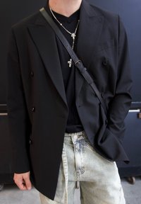 Blazer nero doppiopetto, design elegante con revers testurizzati, abbinato a una camicia nera aderente e jeans in denim chiaro con effetto strappato.