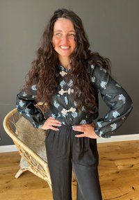 Schwarze Seidenbluse mit blauer floraler Stickerei, langen Ärmeln und dekorativen Knöpfen. Kombiniert mit schwarzen, lässig geschnittenen Hosen.