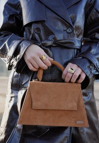 Borsa a tracolla in camoscio marrone con design strutturato e manico superiore, dotata di chiusura a patta e logo argentato nell'angolo in basso a destra.