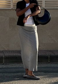 Γκρι εφαρμοστή μακριά φούστα, λευκό μπλουζάκι κάτω από μαύρο κοντομάνικο μπουφάν. Μαύρη τσάντα με καμπυλωτό σχέδιο και μαύρα φλατ παπούτσια με καρφιά.