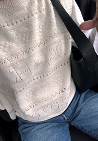 Suéter branco de malha com padrões texturizados, incluindo corações e motivos florais, combinado com jeans azul e uma bolsa preta.