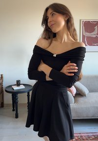 Top negru cu umerii goi, cu design strâns, având un detaliu metalic la decolteu, asortat cu o fustă neagră evazată.