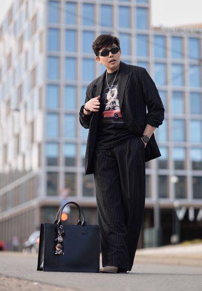 Traje negro a rayas con pantalones a juego, camiseta gráfica negra, joyas de plata y gafas de sol. Bolso de cuero negro con detalle de llavero.