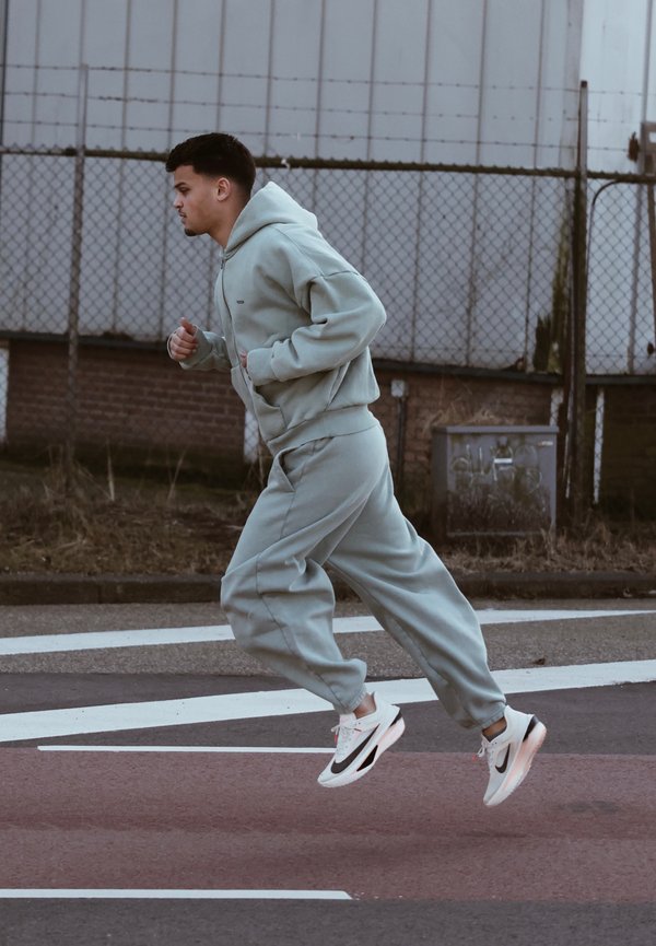 Felpa oversize azzurra chiara e pantaloni jogger in morbido tessuto. Corri con sneakers Nike bianche e nere con suole trasparenti. Sfondo urbano.