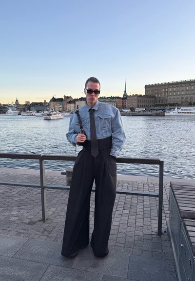 Chaqueta de mezclilla de manga larga, corbata negra y pantalones anchos negros. El conjunto presenta un ajuste relajado y una silueta estructurada.