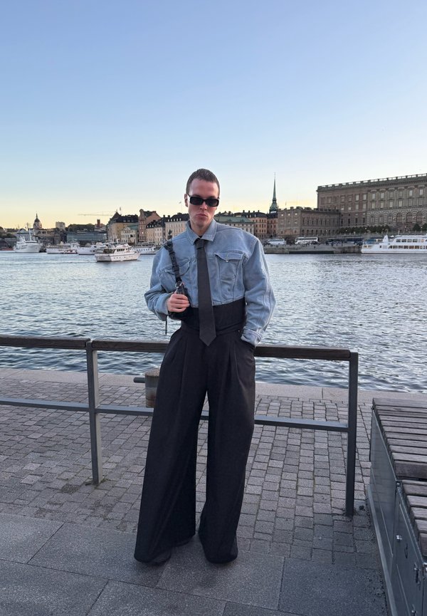 Jachetă din denim cu mâneci lungi, cravată neagră și pantaloni largi negri. Ținuta are un croi lejer și o siluetă structurată.