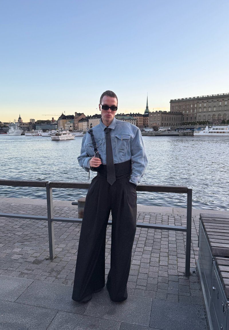 Denimjakke med lange ærmer, sort slips og brede sorte bukser. Outfittet har en afslappet pasform og en struktureret silhuet.