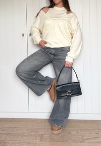 Kremna majica z odkritimi rameni, sive hlače širokih nogavic, bež semiš škornji gležnarji in majhna črna usnjena torbica z zlatim zaponkom.