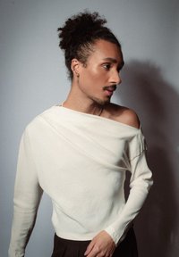 Licht beige lange mouwen shirt met een off-shoulder halslijn, gedrapeerd ontwerp en een gladde textuur, gecombineerd met donkere broek.