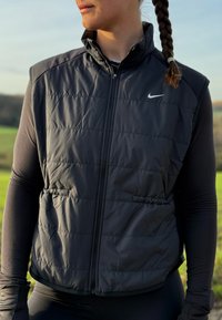 Fekete szigetelt mellény magas gallérral, elöl cipzárral és oldalzsebekkel. Finoman steppelt mintázattal és kis fehér Nike logóval a mellkasnál.