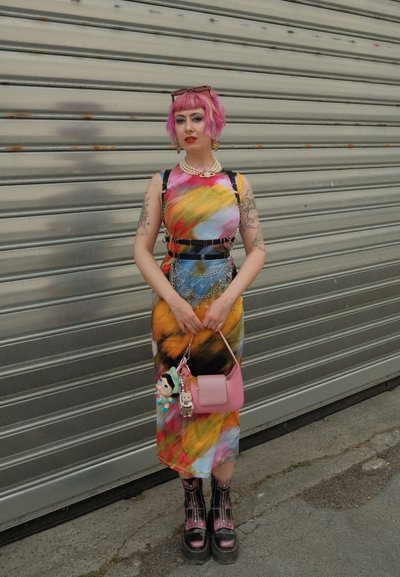 Vestido colorido con patrones abstractos, cinturón negro con cadenas, bolso rosa con charms y botas negras de plataforma gruesa. Pendientes y collar de plata.