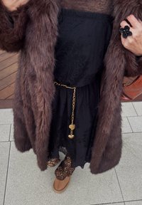 Smeđa lažna krzna jakna preko crne čipkaste haljine, zlatni lančić s privjeskom u obliku srca, i cipele s leopard uzorkom. Tamna torba u ruci.