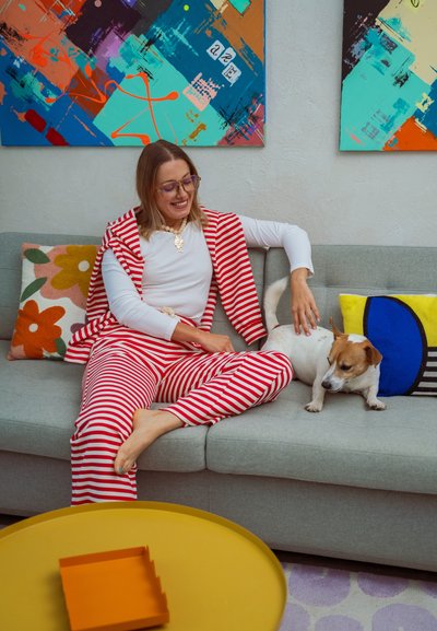 Conjunto de pijama a rayas rojas y blancas, de tela suave y corte relajado. Sofá gris con cojines coloridos. Perro pequeño cerca. Mesa de café amarilla.