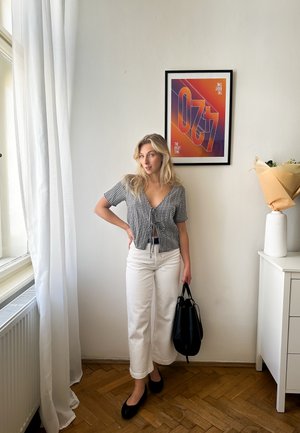 Juodai baltas šachmatų rašto trumpas topas, balti plačios kojos kelnių, juodi butai, laikantys juodą krepšį, fone - spalvingas meno atspaudas ir vaza.