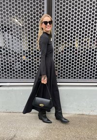 Dolga črna obleka z dolgimi rokavi in pernatimi detajli, v kombinaciji s črnimi gležnjarji in majhno črno torbico z zlatim sponko.