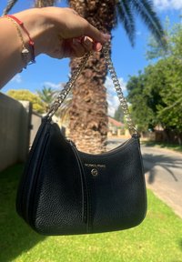 Μαύρη δερμάτινη τσάντα χειρός του Michael Kors με υφή, χρυσή αλυσίδα χερούλι και καμπύλη, δομημένη σιλουέτα.