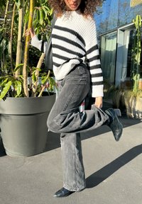 Svart och vitrandig tröja, ribbad textur; högmidjade svarta jeans, utsvängd ben; svarta ankelskotter. Blomkruka i bakgrunden.