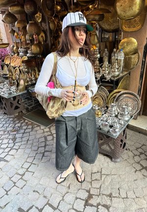 Conjunto casual que incluye una camiseta blanca de manga larga, pantalones cortos de mezclilla negros y una bolsa de camuflaje. Rodeado de decoraciones metálicas y cubiertos de plata.