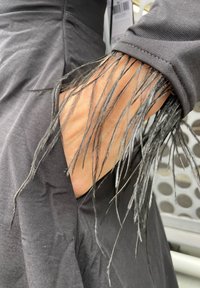 Črna obleka z dolgimi, tankimi črnimi resicami, ki segajo iz rokava, z gladko teksturo in prilegajočo obliko.