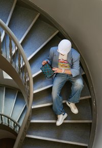 Borsa nera e blu a fantasia tenuta da una persona seduta su una scala a chiocciola, indossando un blazer blu chiaro e jeans di denim.
