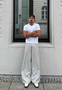 Camisa blanca de manga corta, pantalones grises de gran tamaño y zapatos blancos con detalles marrones, ante un sencillo fondo urbano.
