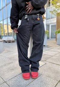 Melnas džinsa bikses ar brīvu piegriezumu, ar aukliņu jostā, sānu kabatām un krāsainiem atslēgu piekariņiem. Kopā ar sarkaniem klogiem.