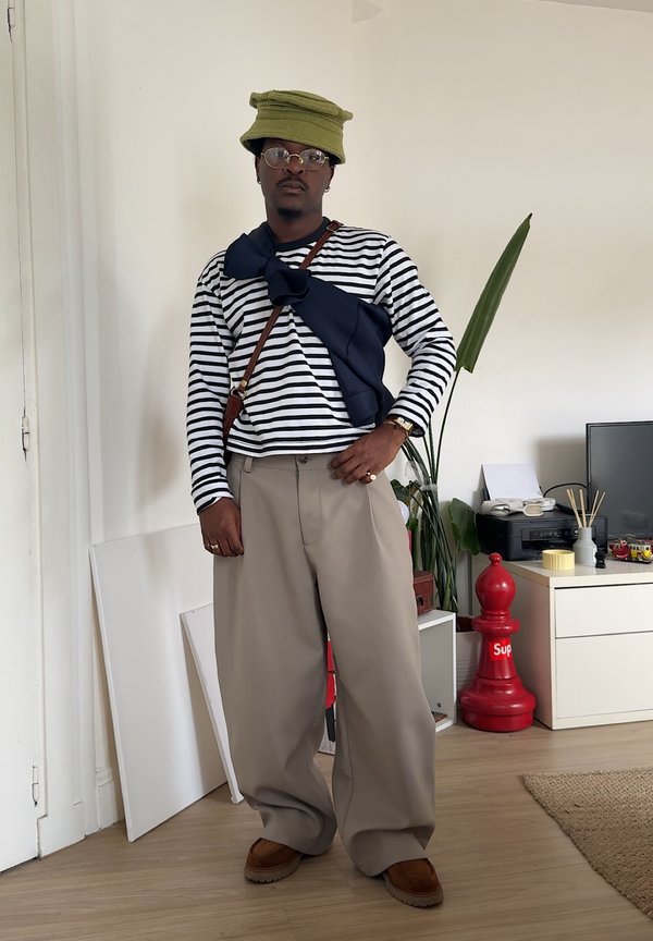 Camisa de manga larga a rayas con acento en navy, pantalones anchos beige, sombrero de cubo verde, gafas y zapatos de tela marrones.