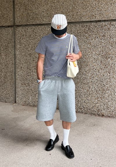 Camiseta a rayas azul marino y blanca, pantalones cortos de sudadera grises, mocasines negros, calcetines blancos y una gorra gris y negra. Bolsa de hombro sólida beige.