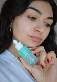 Siero CICALURONIC™ in una bottiglia di vetro satinato azzurro chiaro con un tappo contagocce bianco. Il testo sulla bottiglia descrive i suoi benefici per la pelle secca.