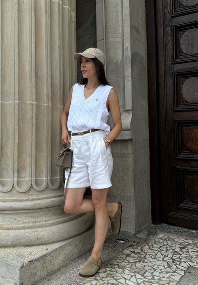 Camiseta sin mangas de punto blanco, pantalones cortos blancos de talle alto, gorra beige, bolso cruzado marrón y zapatos slip-on de ante marrón.