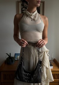 Geantă de umăr din piele neagră cu accesorii din metal argintiu, având o formă curbată și detalii ornate. Top și fustă cu dungi, confecționate dintr-un material ușor.