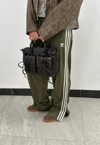 Μαύρη δερμάτινη τσάντα με πολλές τσέπες, υφή επιφάνειας και μακριές λαβές. Φοριέται με ελαιόχρωμα παντελόνια που έχουν λευκές ρίγες.