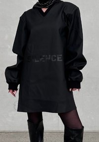 Μαύρο υπερμεγέθες φόρεμα με V-λαιμόκοψη και μακριά μα�νίκια. Περιλαμβάνει ανάγλυφο κείμενο "SILENCE" σε αντίθεση με ματ φινίρισμα. Λείο, υφασμάτινο υλικό.