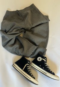 Sive trenerke uparene s crnim visokim Converse tenisicama na bijeloj površini, raspoređene kao da su nosene zajedno.