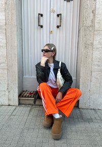 Μαύρο δερμάτινο μπουφάν, λευκή μπλούζα, πορτοκαλί παντελόνι φόρμας με λευκές ρίγες. Φοράει γυαλιά ηλίου, loafers και κρατάει μια μικρή λευκή τσάντα.